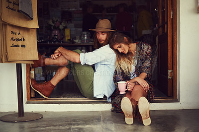 Buy stock photo Shot of an affectionate young couple sitting in the doorway of a roadside shop