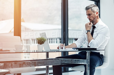 Buy stock photo Shot of a corporate businessman working on a laptop in an office