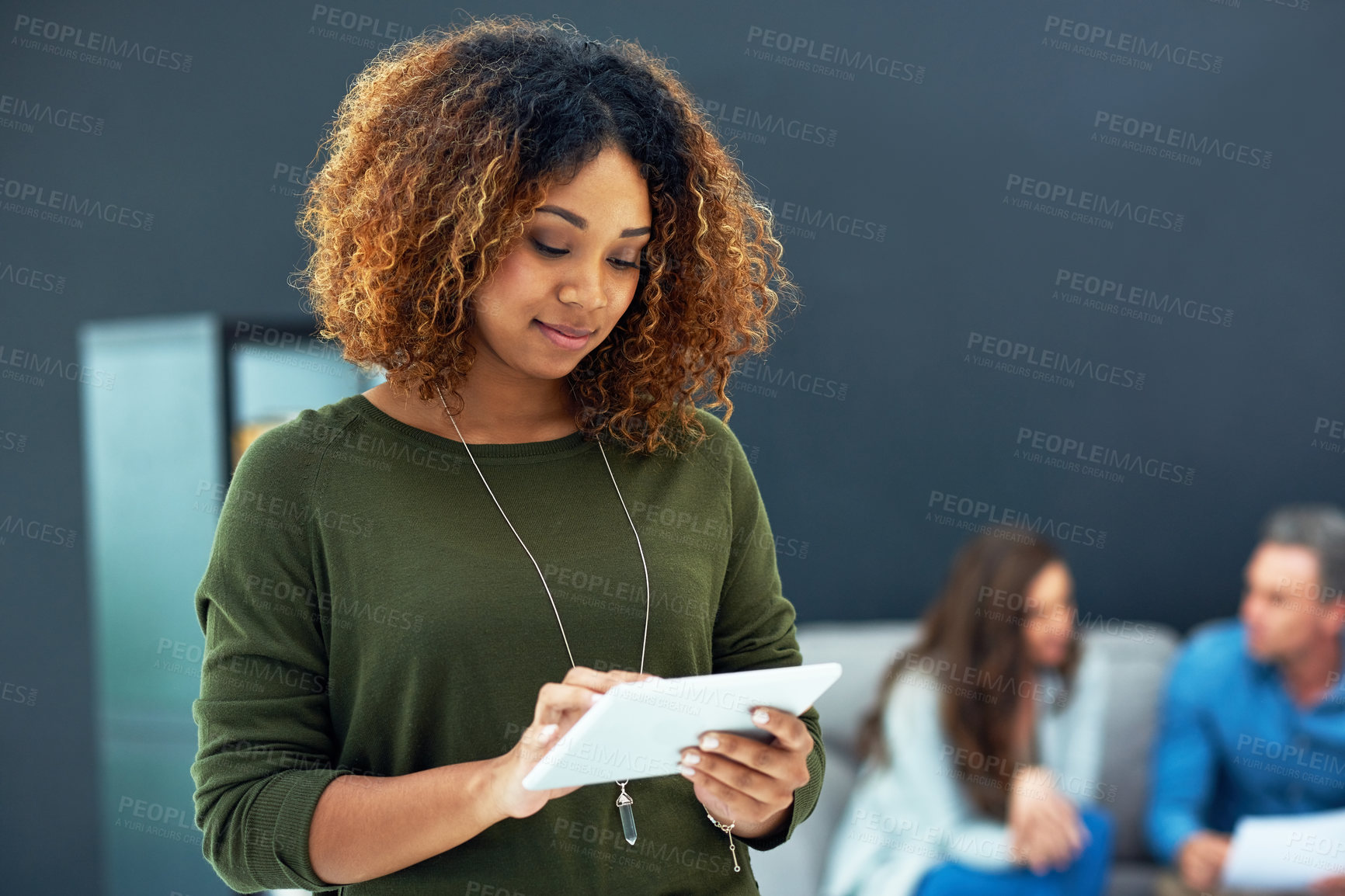 Buy stock photo Shot of a young businesswoman using a digital tablet with her team in the background