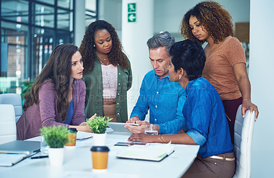 Buy stock photo Shot of a group of designers gathering around a man using a tablet in a meeting