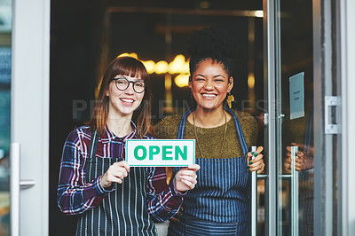 Buy stock photo Shot of two young women holding up an open sign in their coffee shop