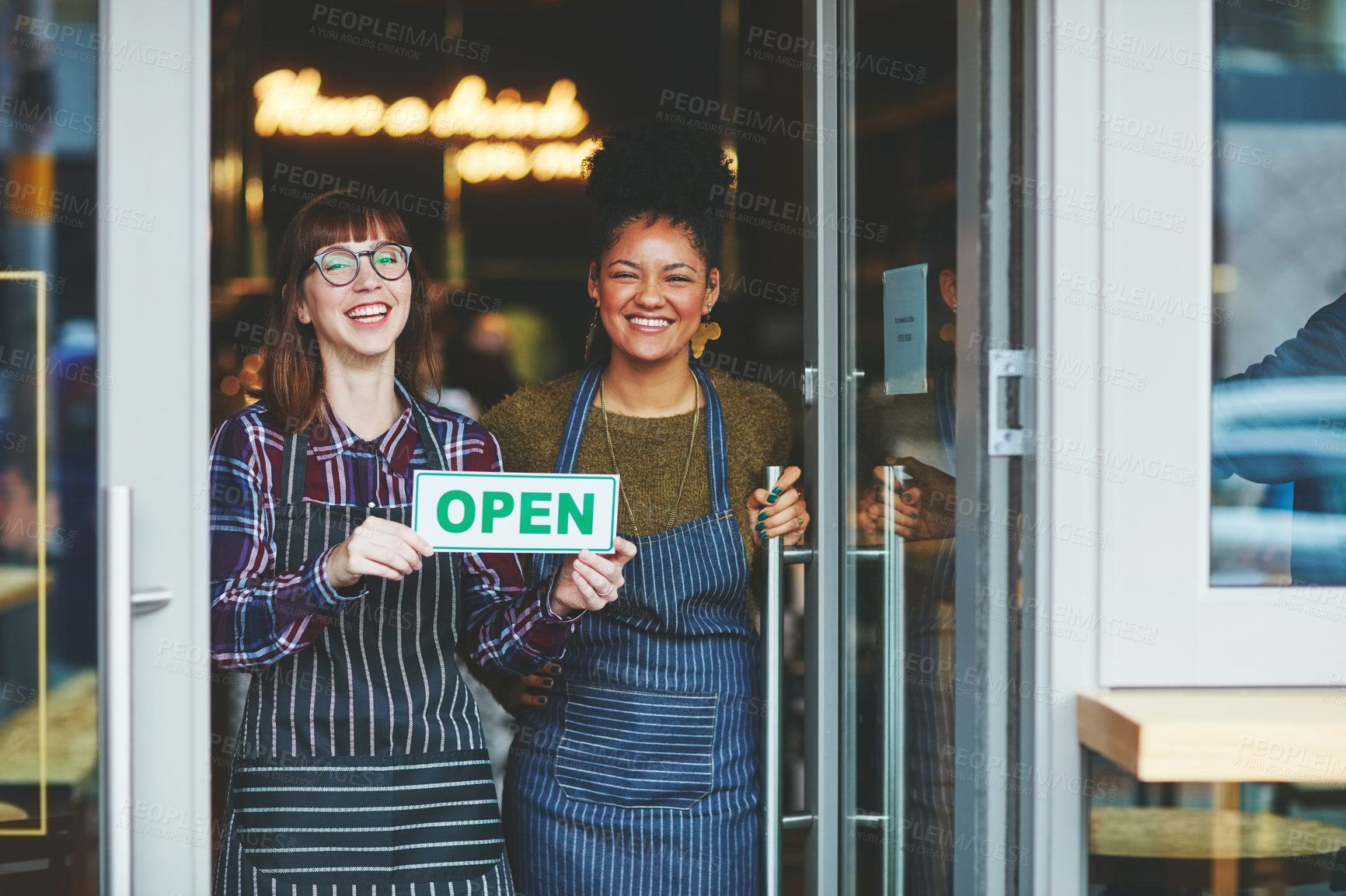 Buy stock photo Shot of two young women holding up an open sign in their coffee shop