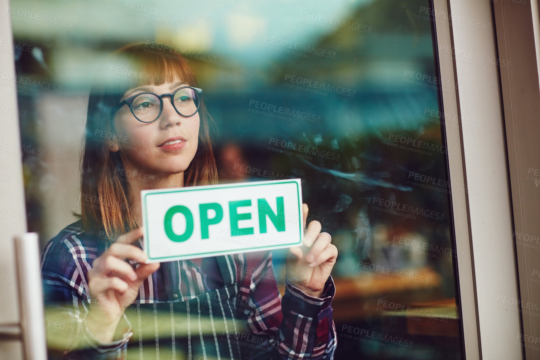 Buy stock photo Shot of a young woman holding up an open sign in her coffee shop