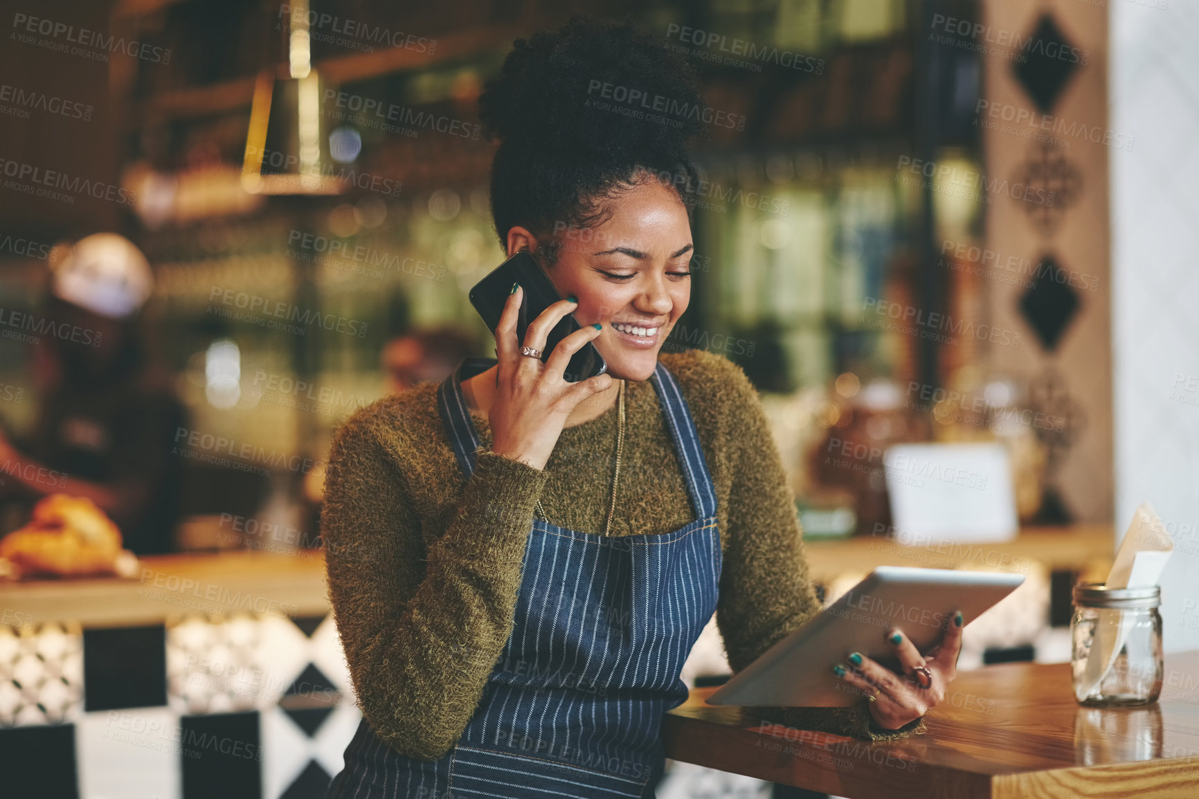 Buy stock photo Shot of a young woman using a phone and digital tablet while working at a coffee shop