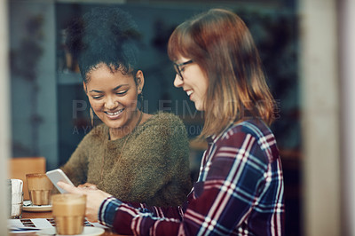 Buy stock photo Cropped shot of two young friends looking at something on a cellphone in a cafe