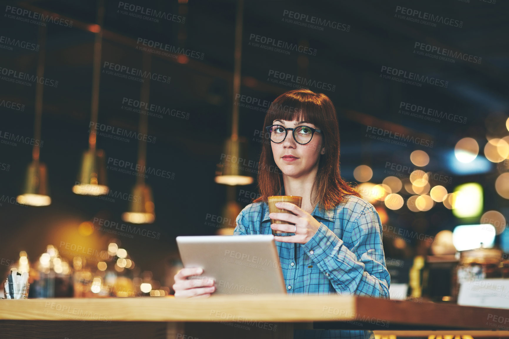 Buy stock photo Shot of an attractive young woman looking thoughtful while using a digital tablet in a cafe