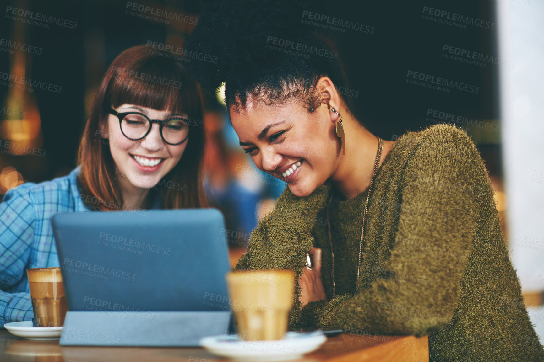 Buy stock photo Shot of two young friends looking at something on a digital tablet in a cafe