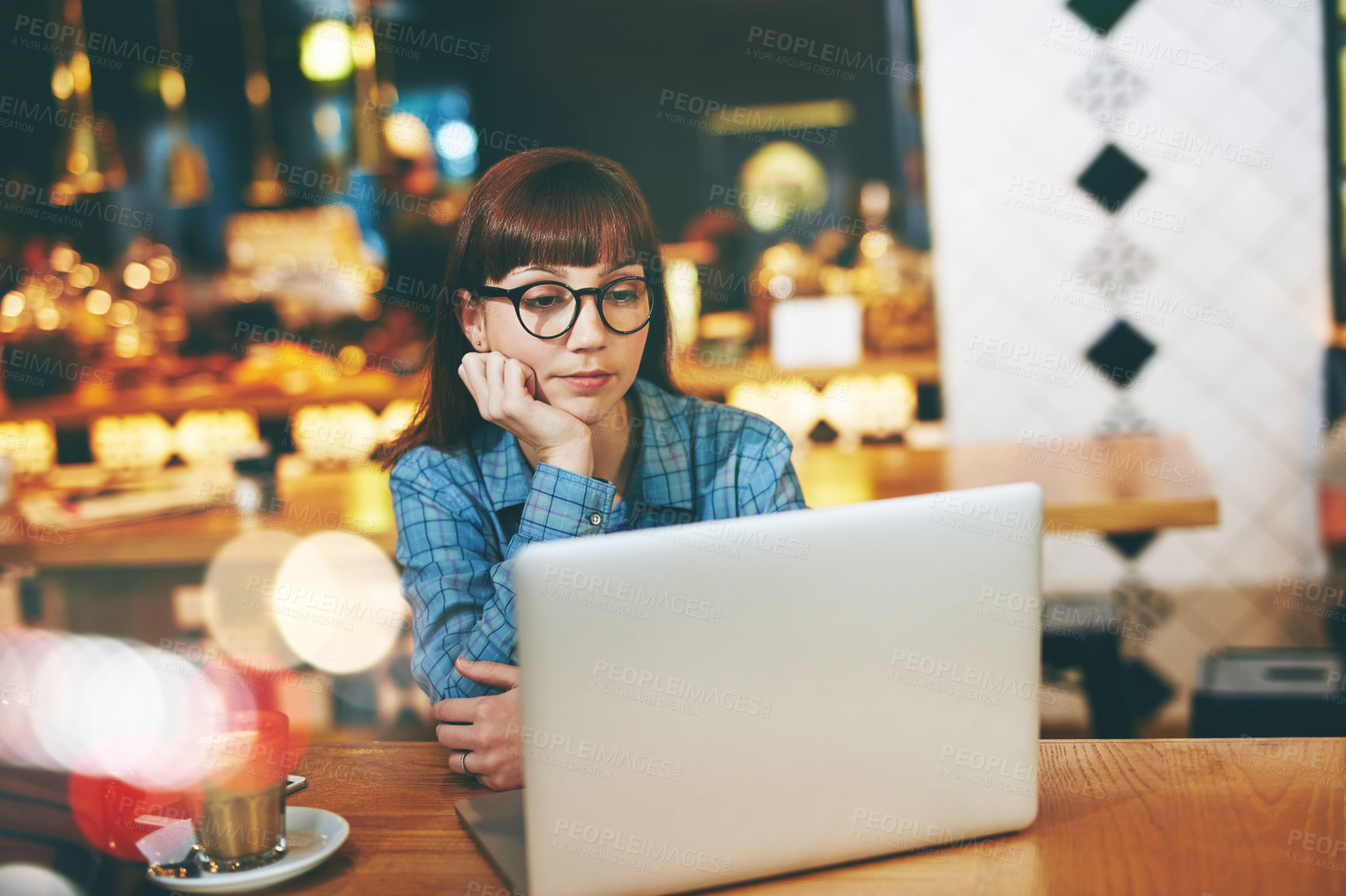 Buy stock photo Shot of an attractive young woman looking thoughtful while using her laptop in a cafe