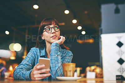 Buy stock photo Shot of an attractive young woman looking thoughtful while texting on her cellphone in a cafe