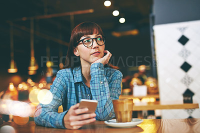 Buy stock photo Shot of an attractive young woman looking thoughtful while texting on her cellphone in a cafe