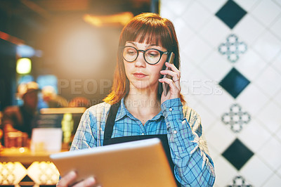 Buy stock photo Shot of a young business owner using a digital tablet while talking on a cellphone in her cafe