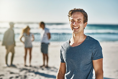 Buy stock photo Portrait of a happy young man posing on the beach with his friends in the background