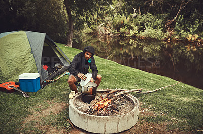 Buy stock photo Camping, cooking and man in forest with fire for adventure, travel and vacation by lake. Wellness, breakfast and male person in nature for eating, nutrition and reflection of trees in water or river