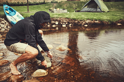 Buy stock photo Shot of a young man filling water from a lake into a pot at a campsite