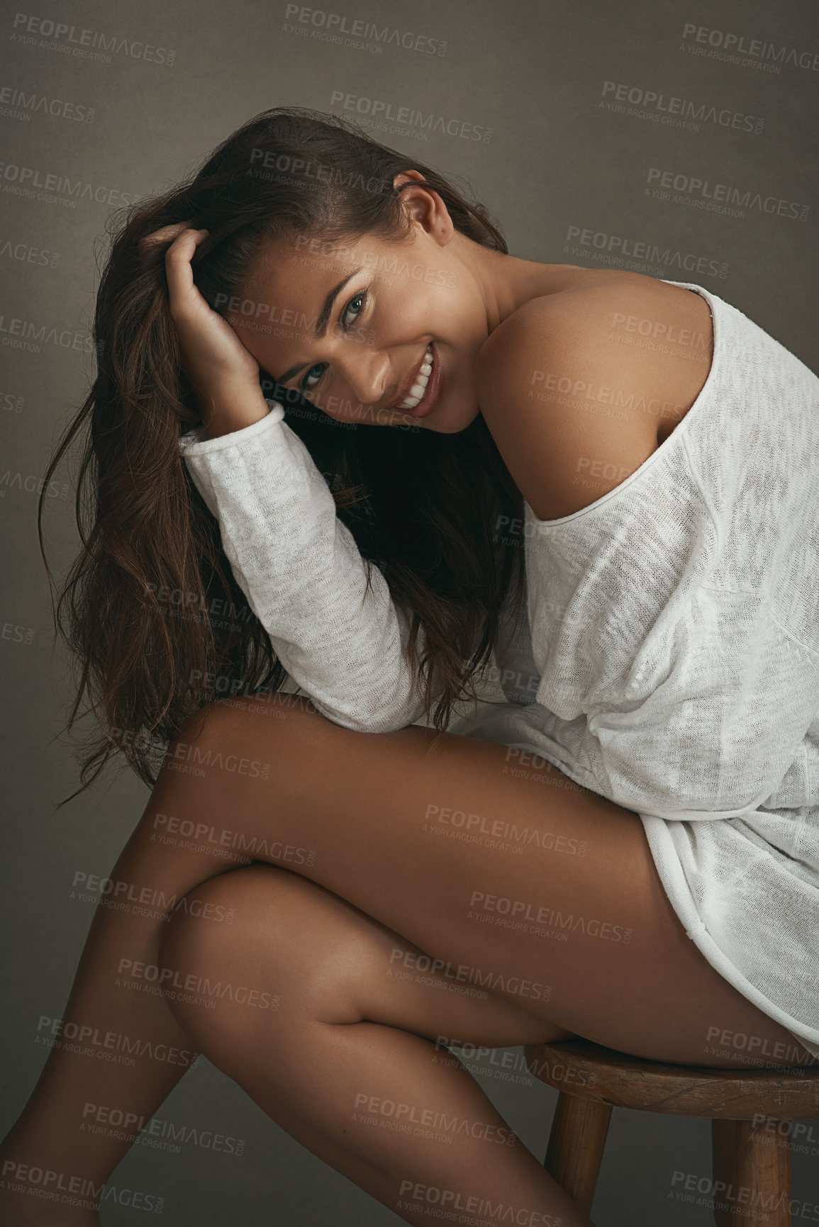 Buy stock photo Portrait of a beautiful young woman sitting on a stool against a brown background in studio