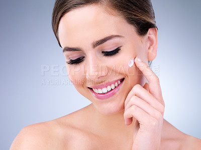 Buy stock photo Cropped shot of a young woman applying moisturizer to her face