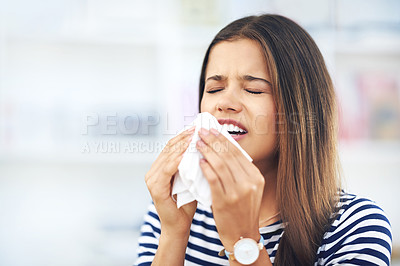 Buy stock photo Shot of a young woman with allergies sneezing into a tissue at home