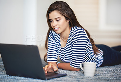 Buy stock photo Shot of a smiling young woman lying on the floor at home using a laptop