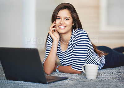 Buy stock photo Portrait of a smiling young woman lying on the floor at home using a laptop