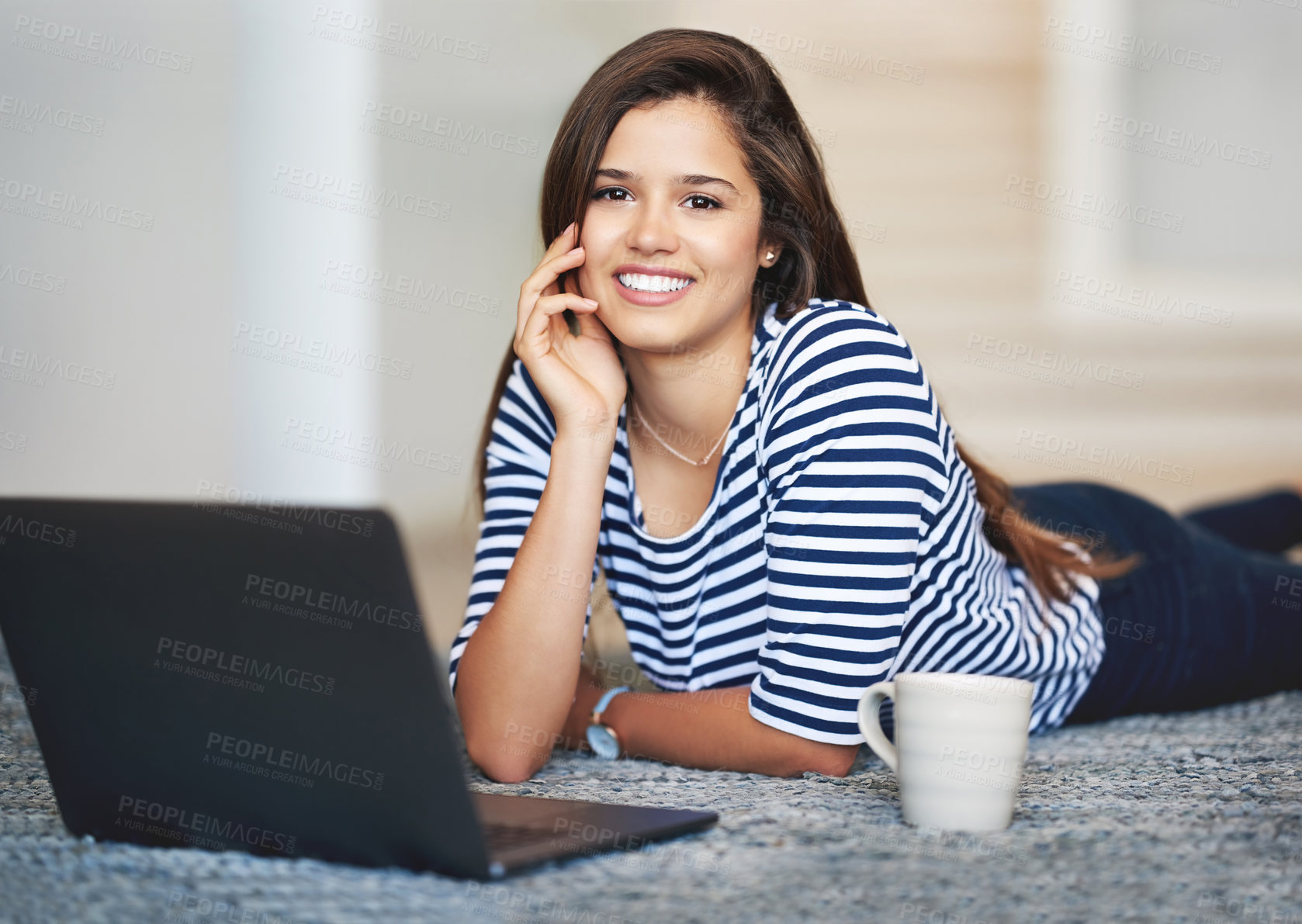 Buy stock photo Portrait of a smiling young woman lying on the floor at home using a laptop