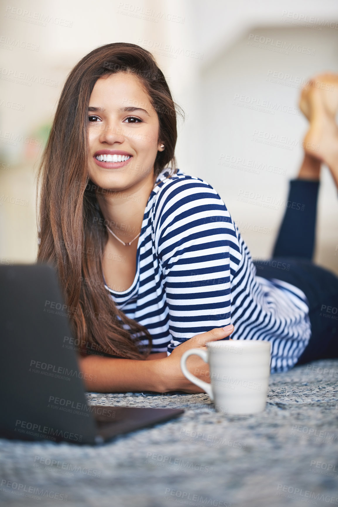 Buy stock photo Portrait of a smiling young woman lying on the floor at home using a laptop