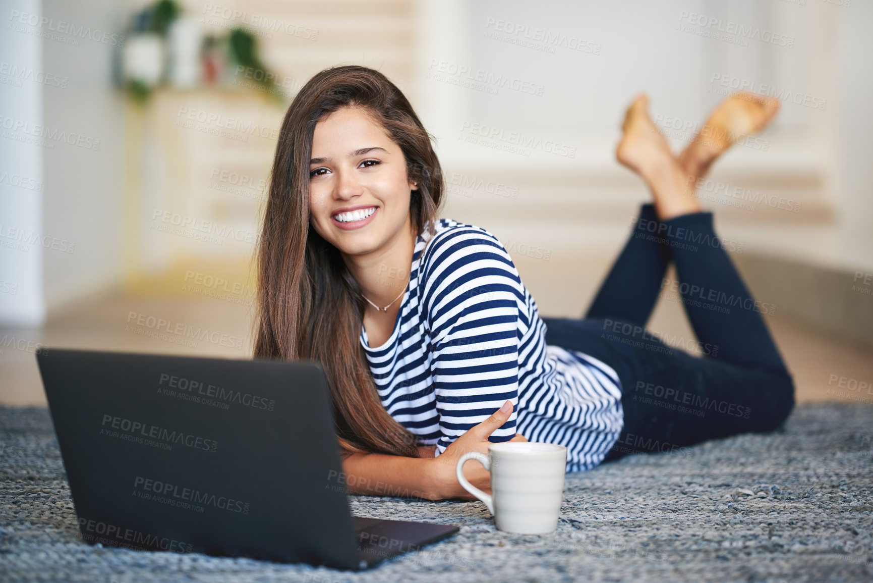 Buy stock photo Portrait of a smiling young woman lying on the floor at home using a laptop