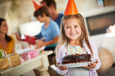 Buy stock photo Shot of a happy little girl holding a birthday cake with her family in the background