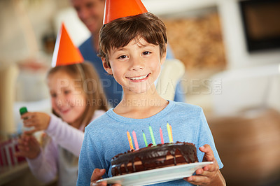 Buy stock photo Portrait of a happy little boy holding a birthday cake with his family in the background