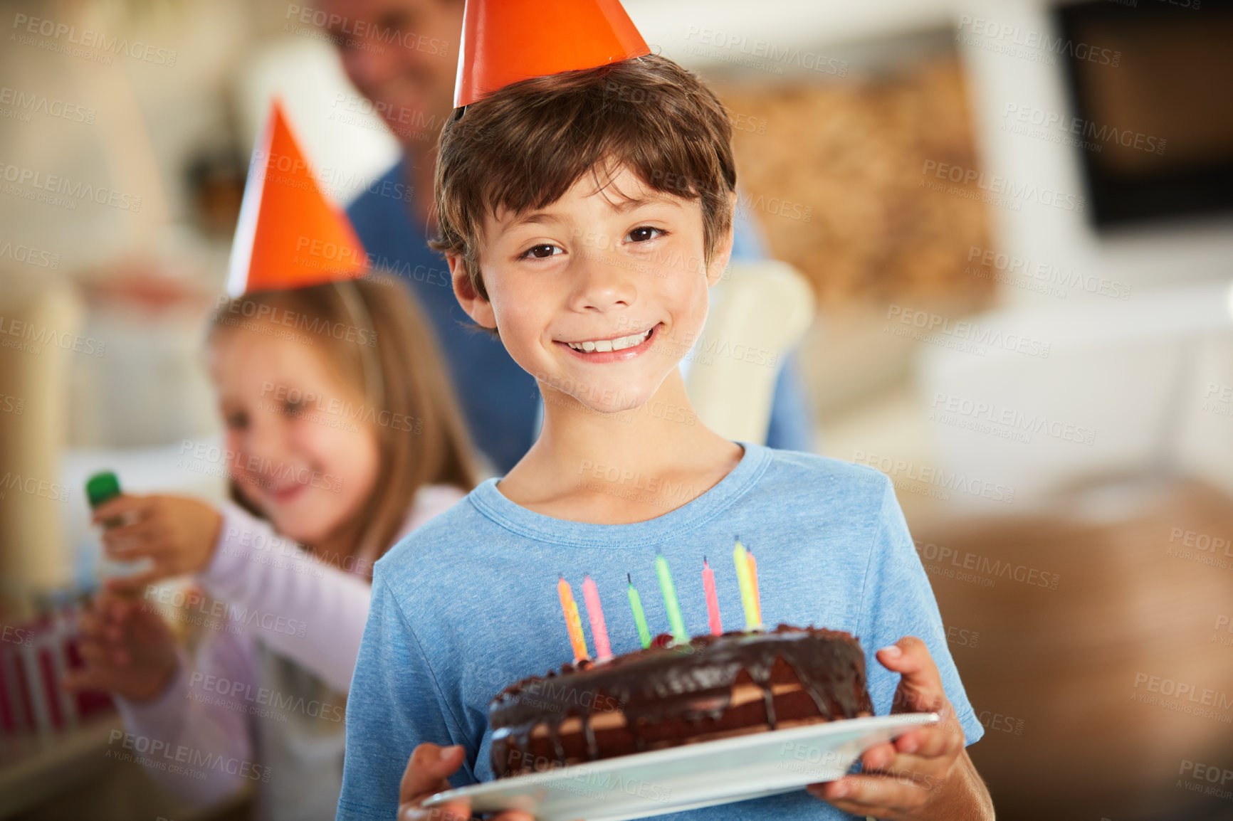 Buy stock photo Portrait of a happy little boy holding a birthday cake with his family in the background