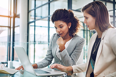 Buy stock photo Shot of two young businesswomen using a laptop together at work