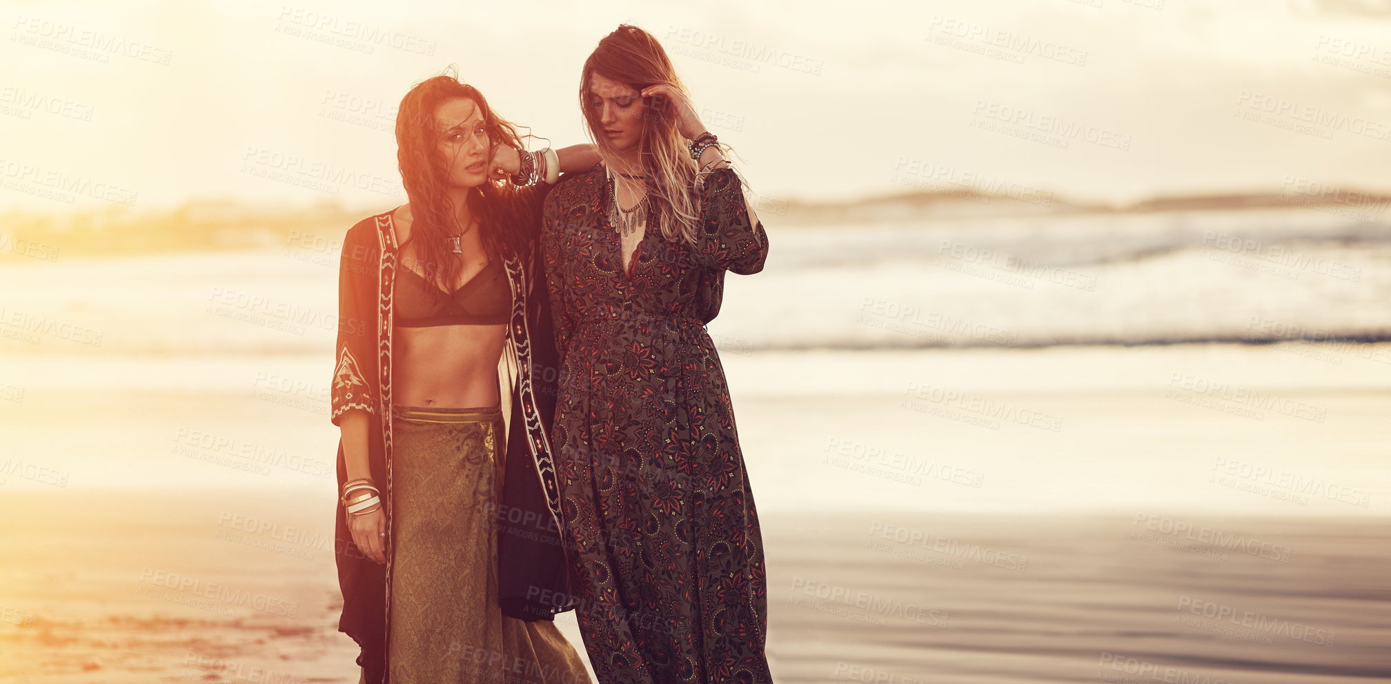 Buy stock photo Shot of two young women spending the day at the beach at sunset