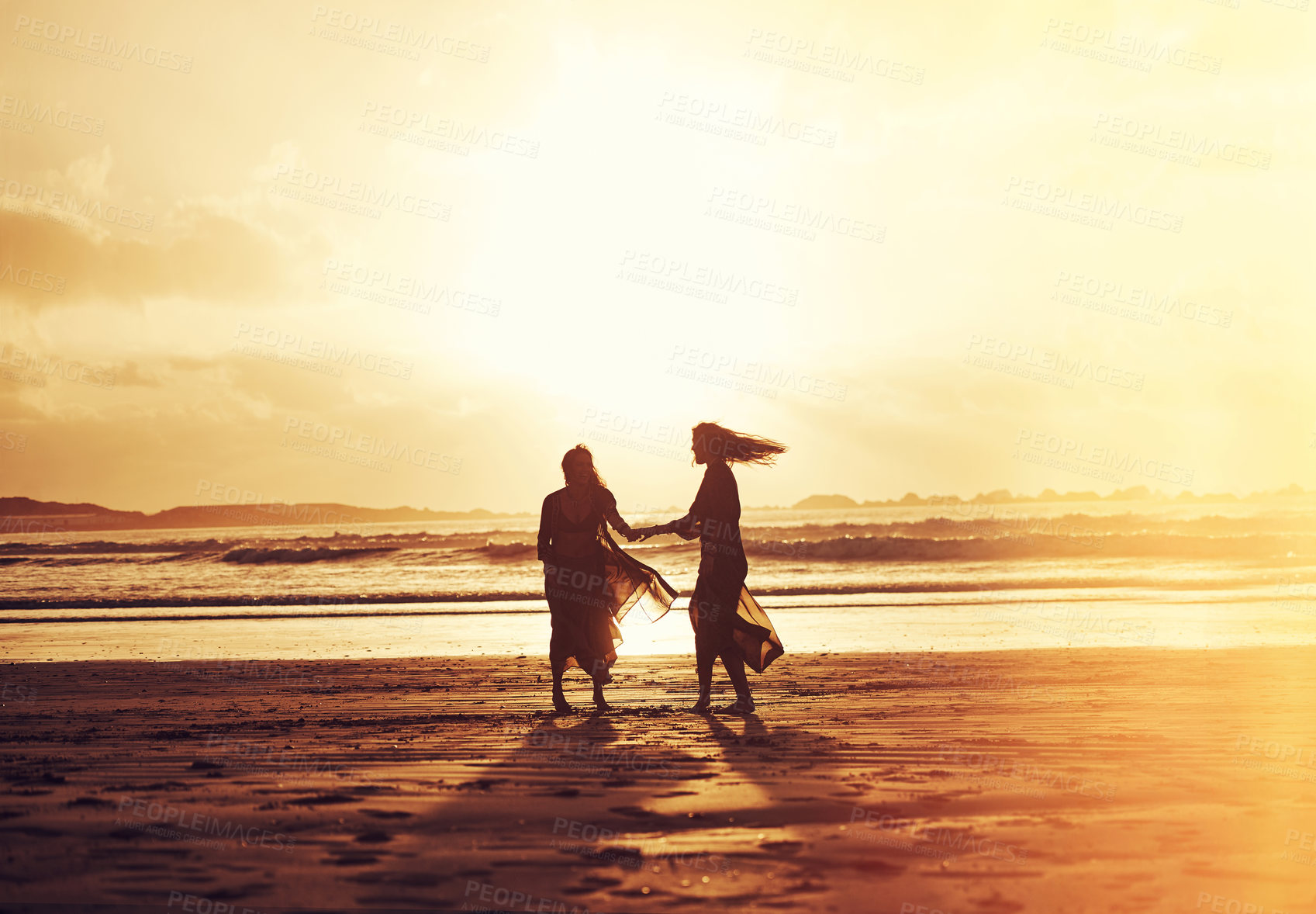 Buy stock photo Shot of two young women spending the day at the beach at sunset