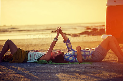 Buy stock photo Shot of an affectionate young couple holding hands while lying on the beach