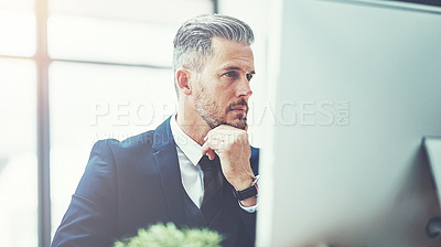 Buy stock photo Shot of a mature businessman using a computer at his desk in a modern office