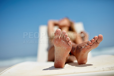 Buy stock photo Close-up of a woman relaxing on a sun bed with adhered sand on her feet. Selective focus on the foot with the sea and raised arm of a woman in the background. Bare feet of a woman with white sand.