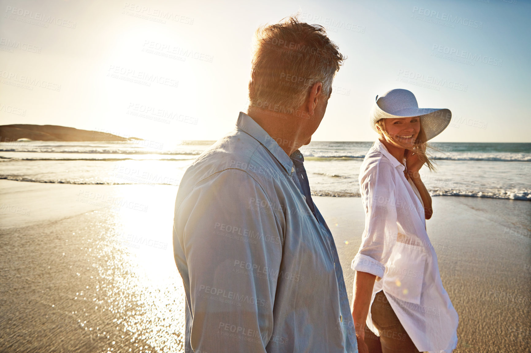 Buy stock photo Senior, happy couple and walking with beach sunset for love, embrace or bonding together in nature. Man, woman or lovers holding hands with smile for summer holiday by water, sea or ocean coast