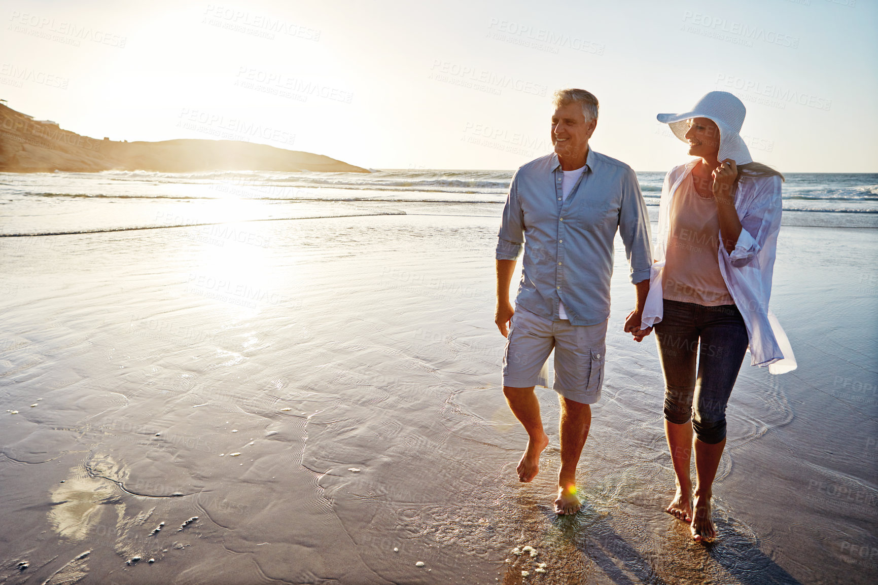 Buy stock photo Mature, happy couple and walking with holding hands in beach sunset for love or bonding together in nature. Man, woman or lovers enjoying stroll on water for outdoor holiday or summer by ocean coast