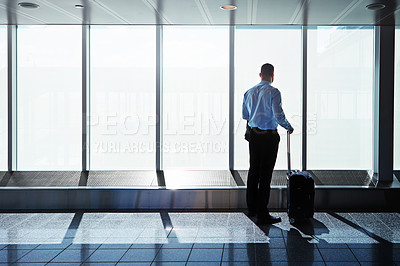 Buy stock photo Shot of a businessman looking through airport windows while on a business trip