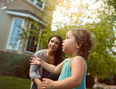 Buy stock photo Cropped shot of a mother and her adorable little daughter playing with bubbles outside