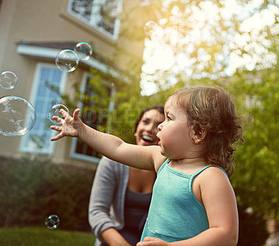 Buy stock photo Cropped shot of a mother and her adorable little daughter playing with bubbles outside