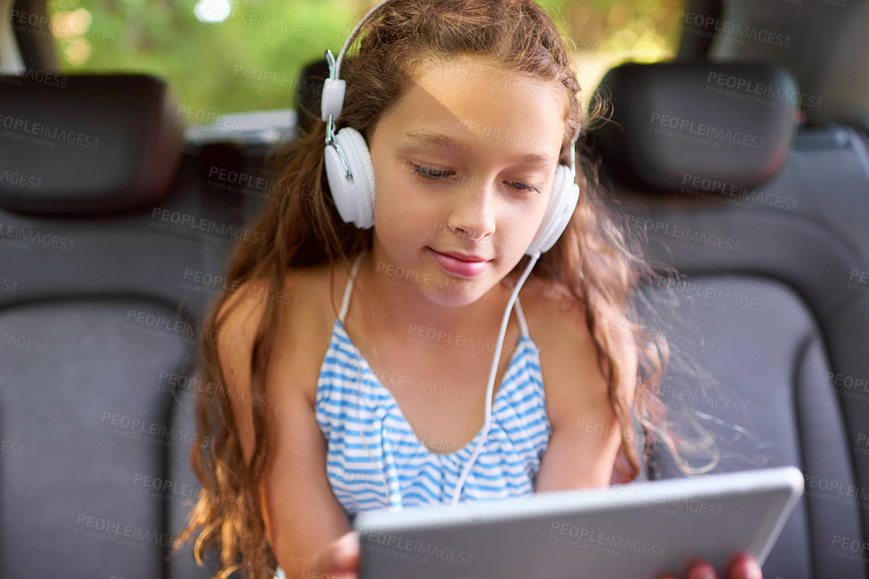 Buy stock photo Girl, child and tablet with headphones in car for video, streaming or movies on family road trip. Kid, happy and watch cartoon with subscription, sound and travel with digital touchscreen with app