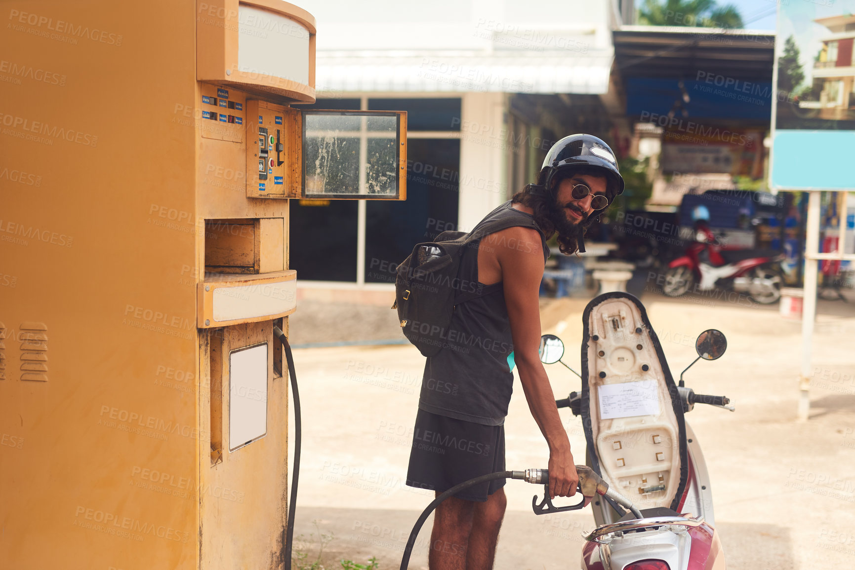 Buy stock photo Shot of a young tourist refueling his scooter at a gas station while exploring a foreign city