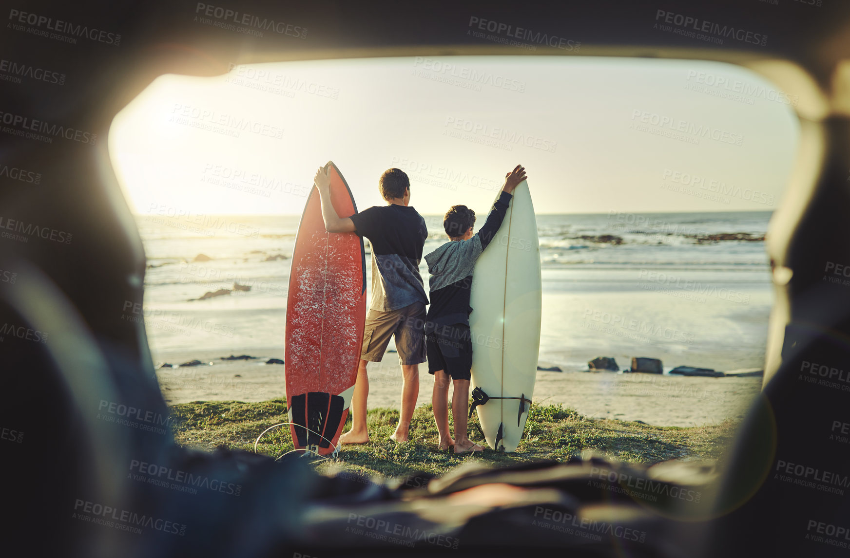 Buy stock photo Rearview shot of two brothers holding their surfboards while standing on the beach