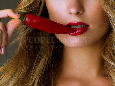 Buy stock photo Cropped studio shot of a young woman eating a red chili suggestively against a dark background