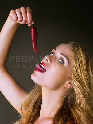 Buy stock photo Studio shot of a gorgeous young woman eating a red chili suggestively against a dark background