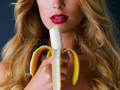 Buy stock photo Cropped studio shot of a young woman eating a banana suggestively against a dark background