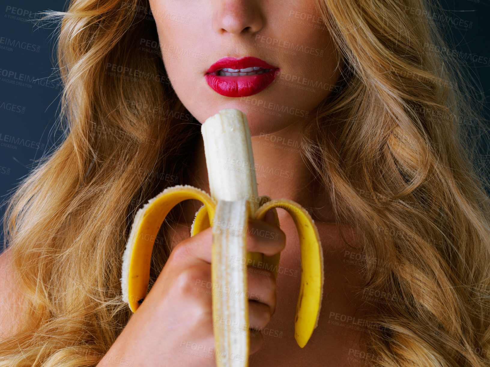 Buy stock photo Cropped studio shot of a young woman eating a banana suggestively against a dark background