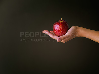 Buy stock photo Giving, hand and red apple in studio for nutrition, wellness and healthy living with vitamin c for diet. Mockup, organic and forbidden fruit of knowledge, temptation and person by dark background