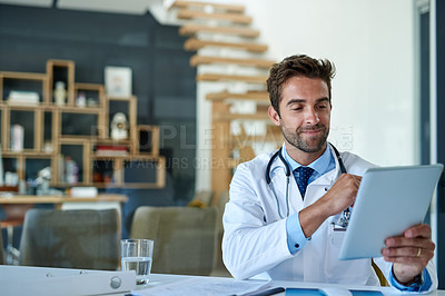 Buy stock photo Cropped shot of a young doctor working on a digital tablet in his office