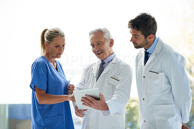 Buy stock photo Cropped shot of a group of medical practitioners discussing something on a digital tablet together